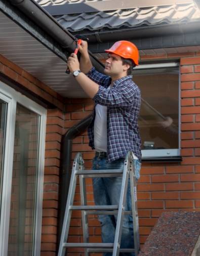 worker standing step ladder repairing gutter house